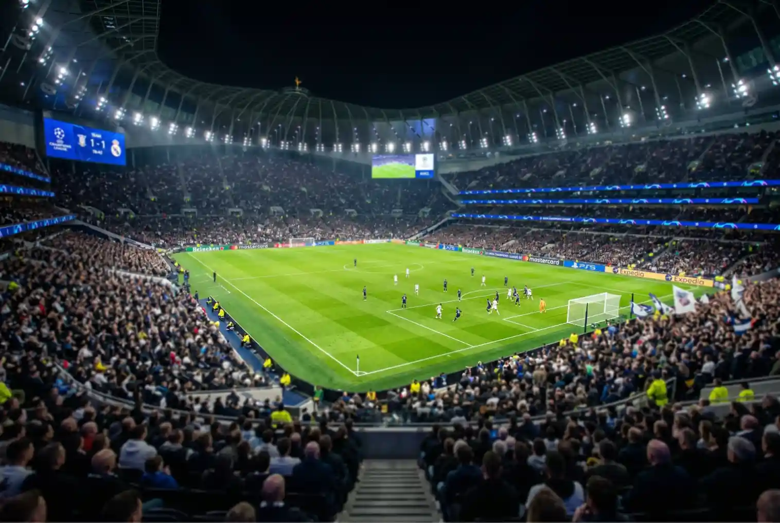 Estadio de fútbol iluminado durante un partido nocturno de la UEFA Champions League con jugadores en el campo verde